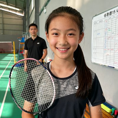15岁学员王悦的肖像照，扎着马尾辫，手持羽毛球拍微笑站在伟德体育场馆内，身后是她的私教教练和训练计划白板。